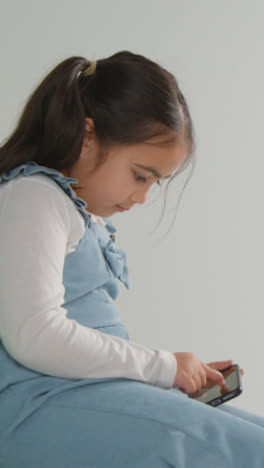 Vertical-Video-Studio-Shot-Of-Young-Girl-On-ASD-Spectrum-Gaming-On-Mobile-Phone-Against-White-Background-1